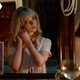 Anya Taylor-Joy puts on an earring while looking in the mirror, which also holds a photo of herself, as Thomasin McKenzie looks at her in Last Night In Soho.